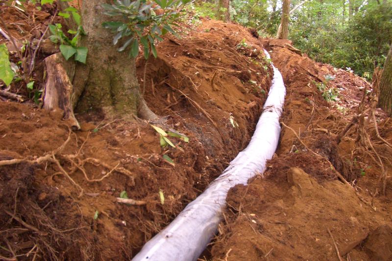 Drain line laid in a narrow trench cut into a red clay slope